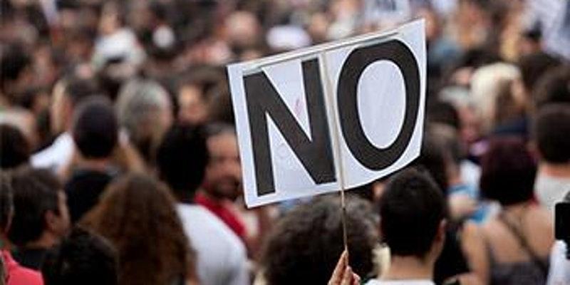 photo of a crowd with a person holding up a sign that says 'NO'