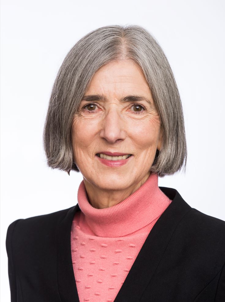 person smiling at camera, with bob hair cut, dressed in black blazer and pink turtle neck 
