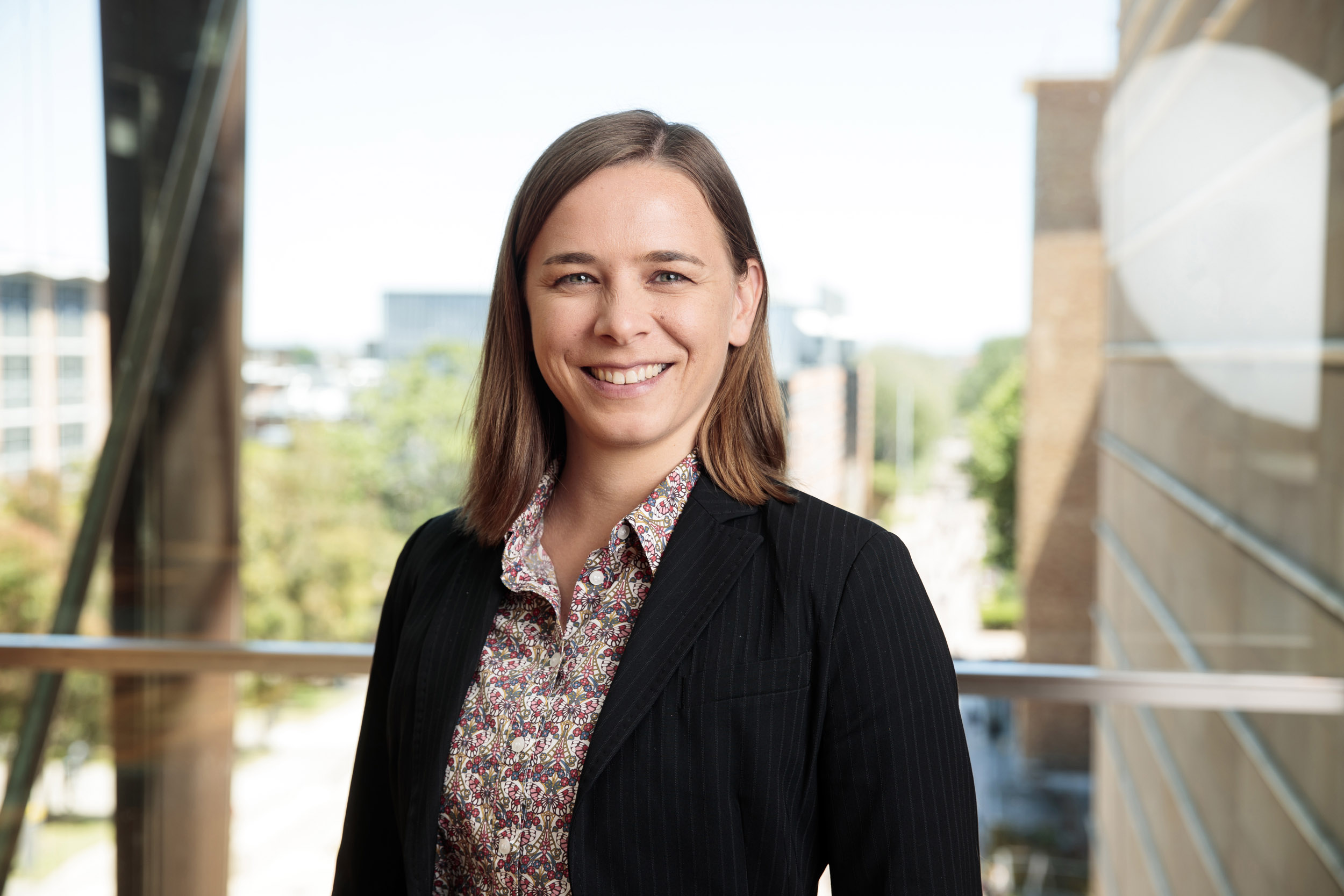 Professor Lisa Harvey-Smith is smiling at the camera. She has shoulder length, straight brown hair. She is wearing a black blazer. 