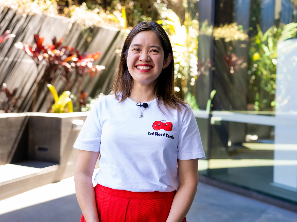 Woman smiling, wearing a white shirt that with a 'Red Blood Comic' logo on it.