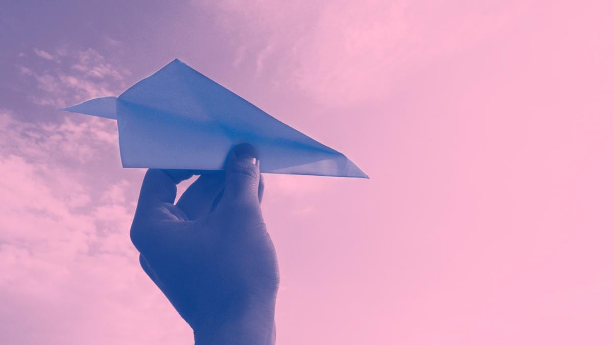 hand throwing a paper airplane in a pink sky