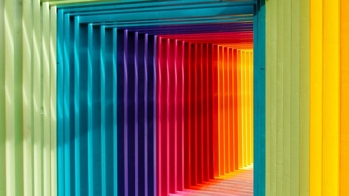 A winding passageway made of wood in rainbow colours. 