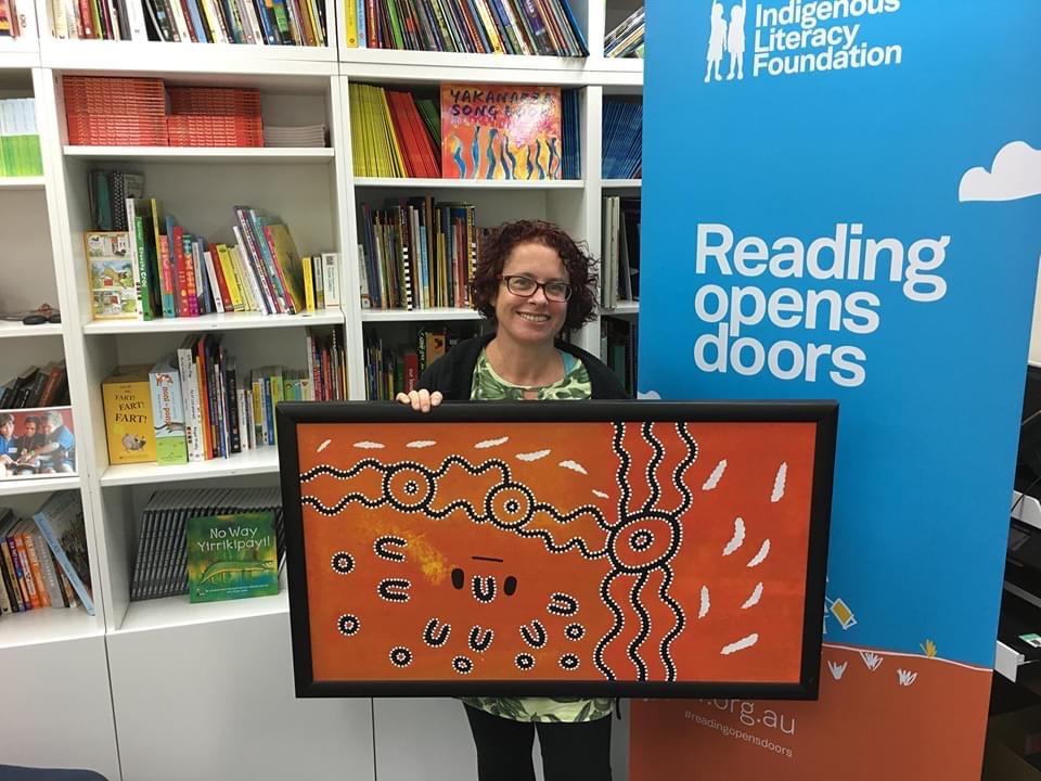 Photo of a women holding a artwork infront of  a bookcase 