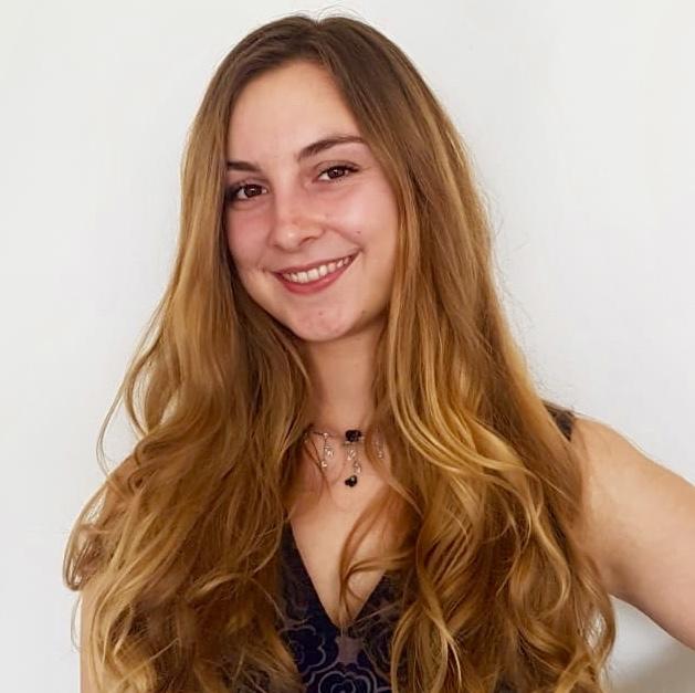 woman with long brown hair, smiling at the camera with hands on hips