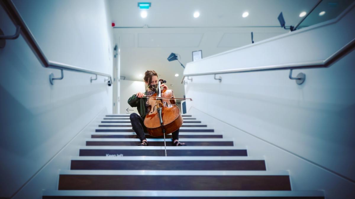 cellist playing on a set of stairs in a white building 