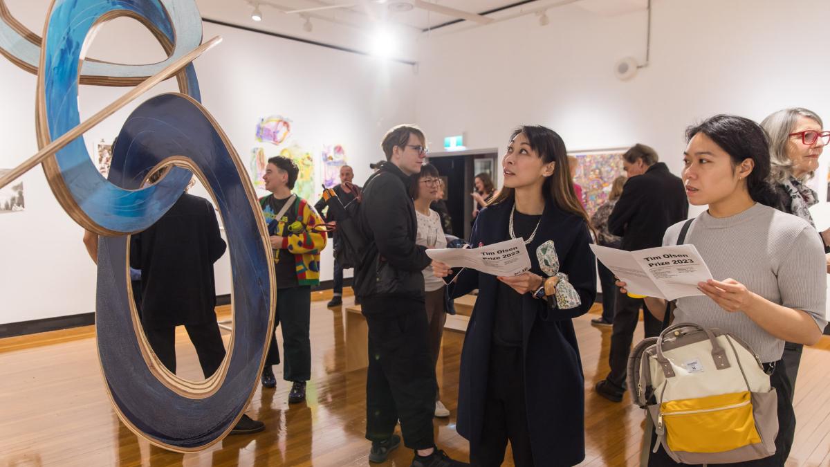 A group of people looking at an exhibition of artworks in a gallery space.