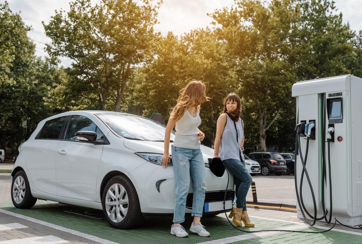 Two ladies leaning on a car hood at an Electric Vehicle charger