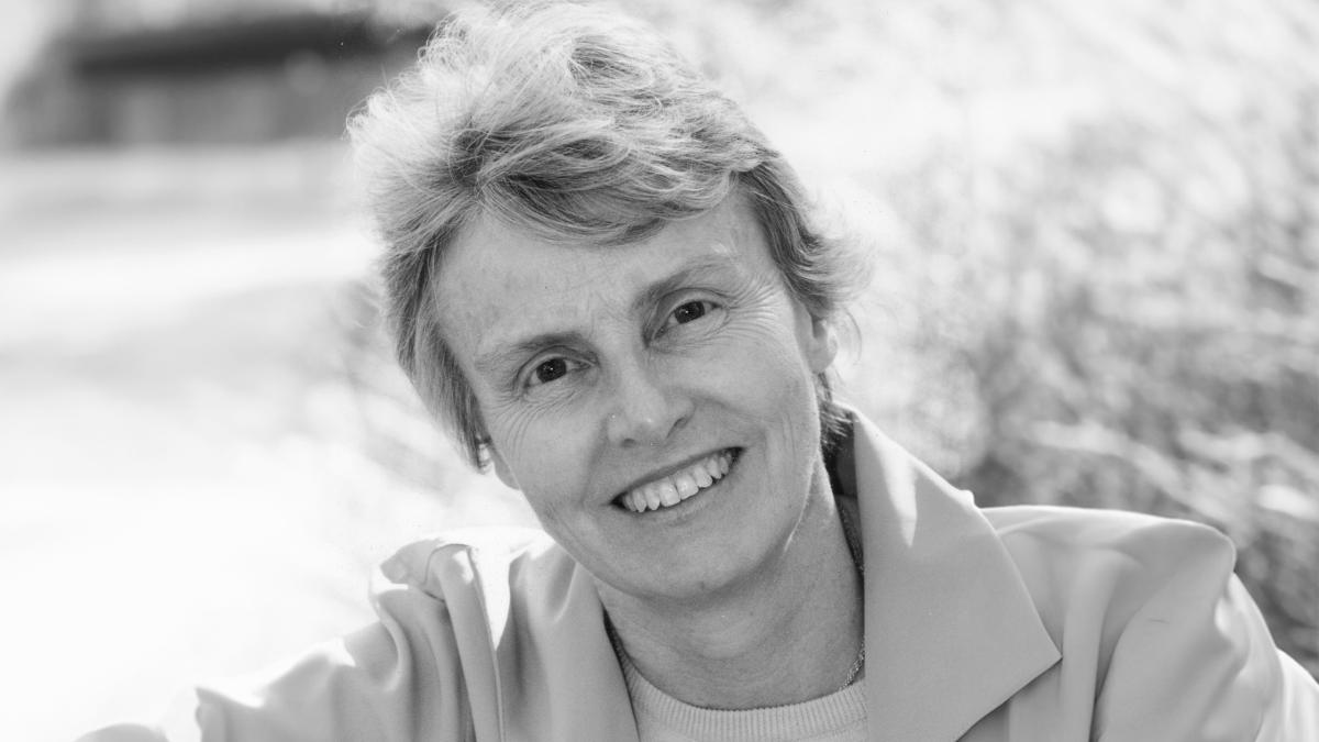 A black and white photo of a woman with light hair, smiling at the camera