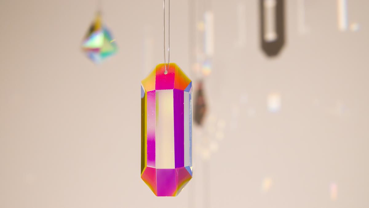 A suspended prism on display in the libraries current display “Colour: Inflections and refractions”, captures and scatters light creating a display of colours.