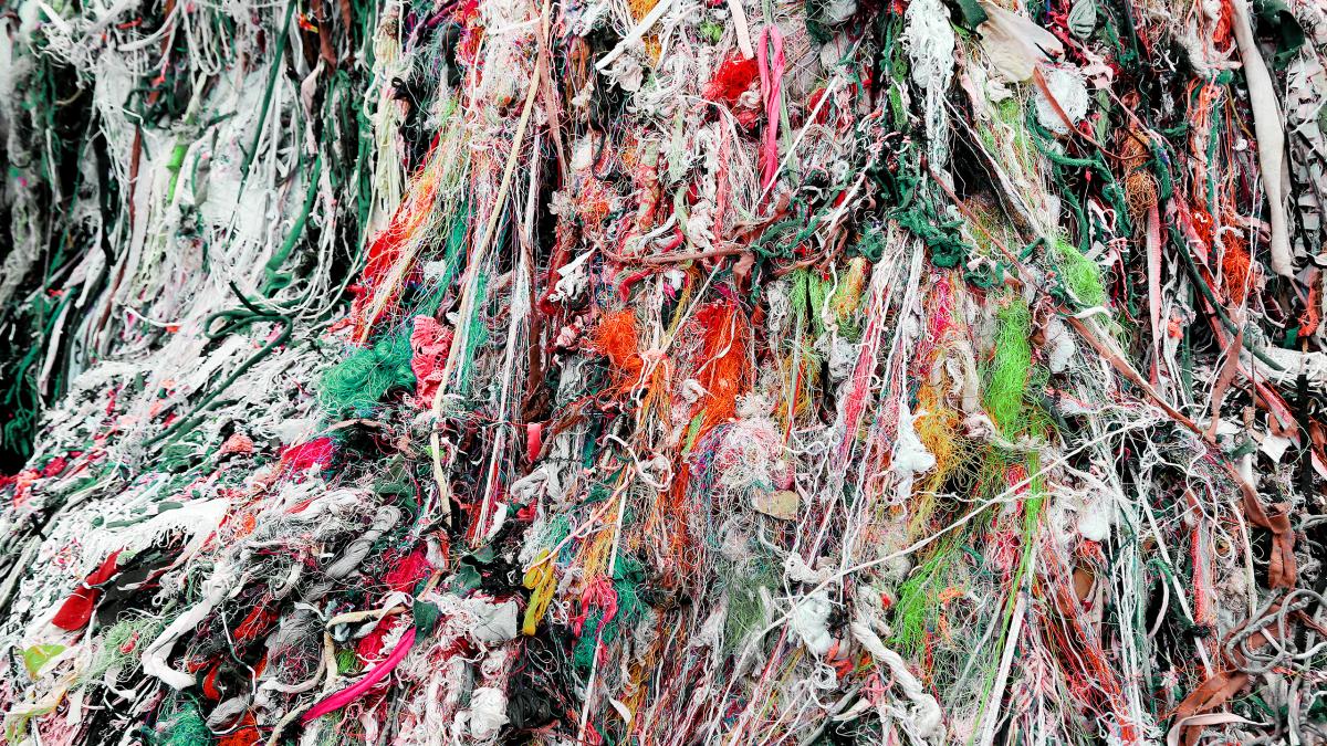 A close-up of a large tangled mass of multicolored threads, fabric scraps, and textile waste