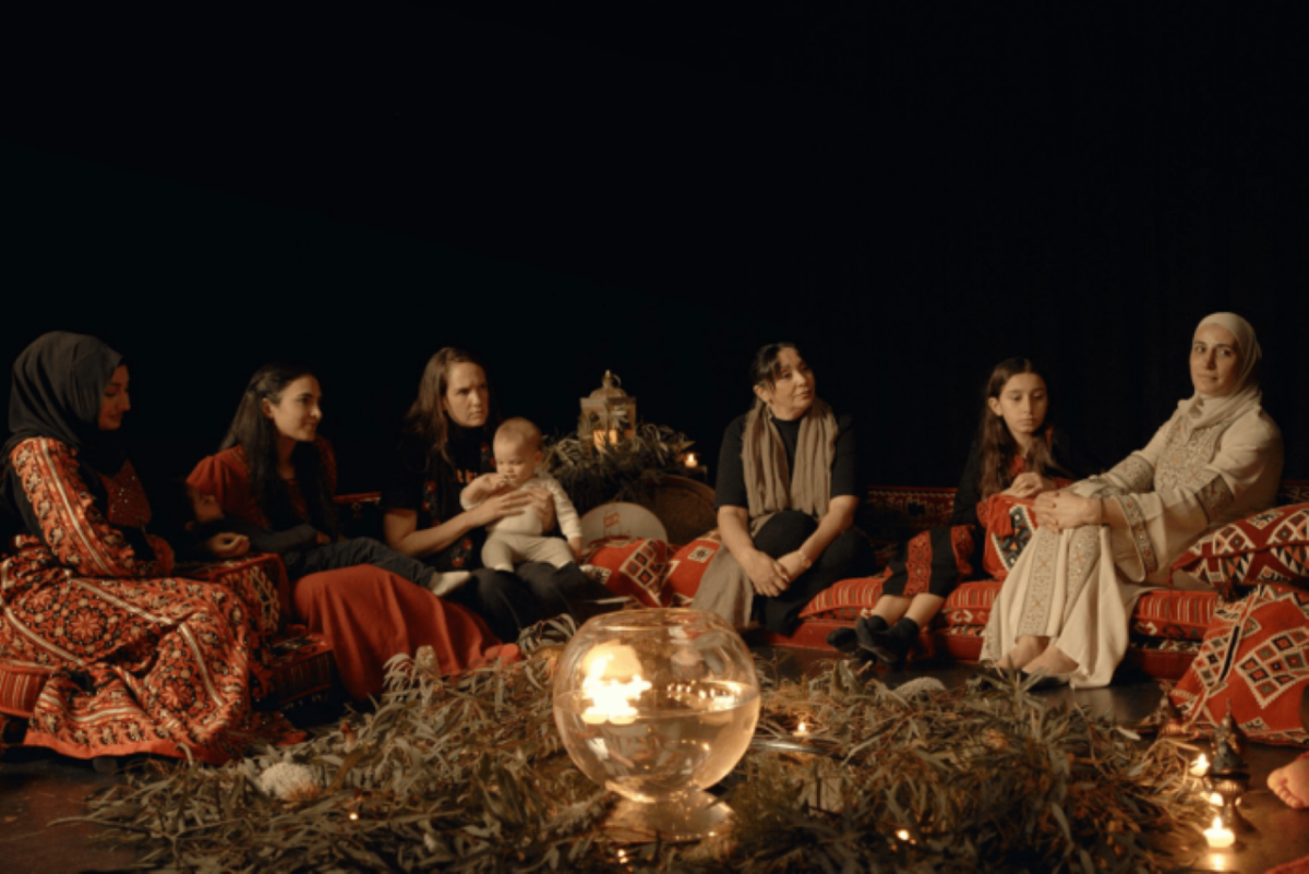 A still from the film Motherhood in the Colony showing a group of women sitting by the fire