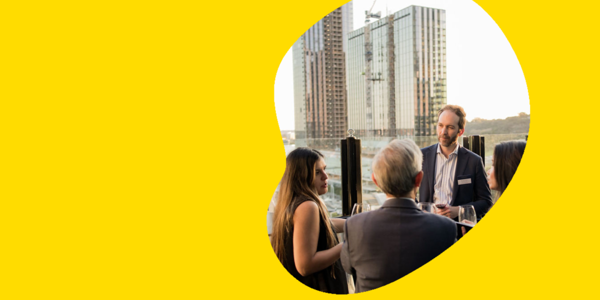 A photograph of 4 alumni chatting on a rooftop terrace at sunset. They are visibly wearing name tags. 