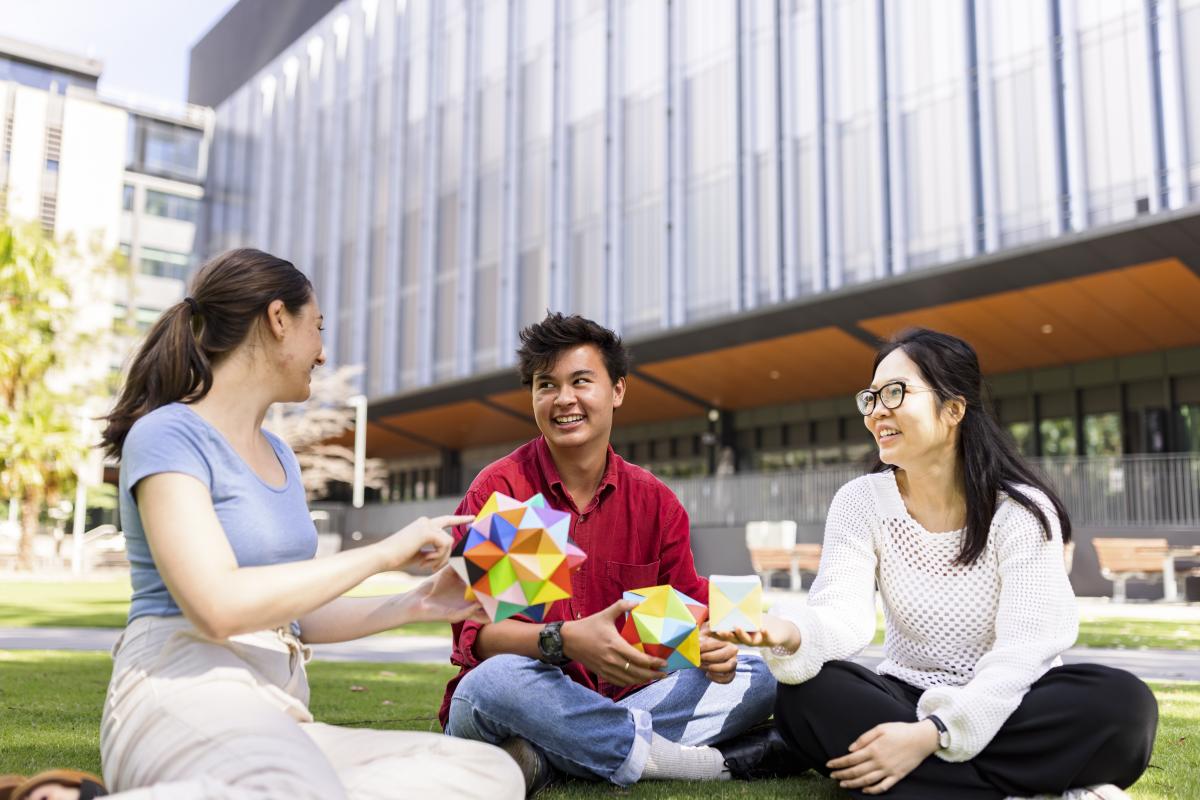 Three students sitting outside on the grass