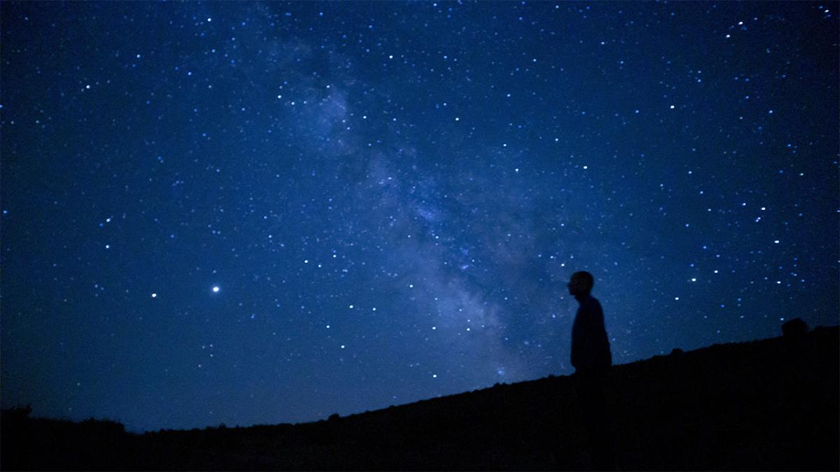 A silhouette of a person looking up at a vast, star-filled night sky and the Milky Way.