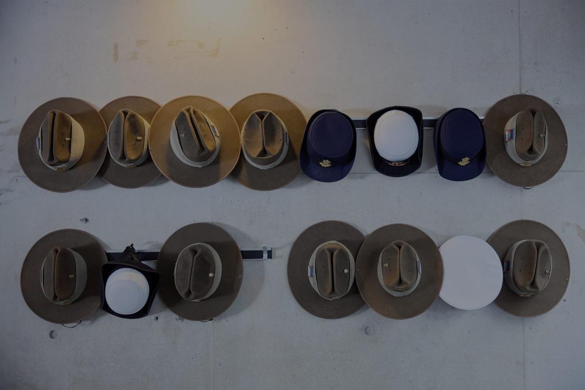 Military hats from all Australian military branches hanging in two rows against a white wall.