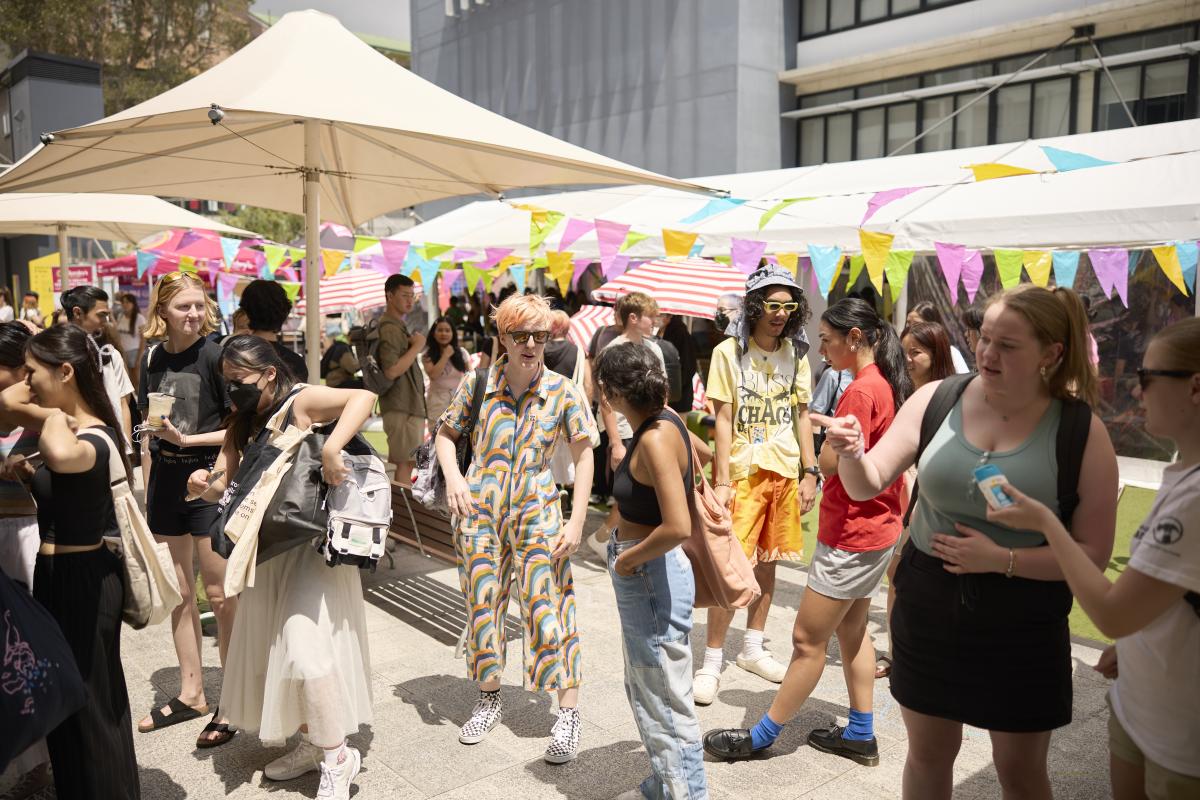 a crowd of students gather round stalls on a sunny day